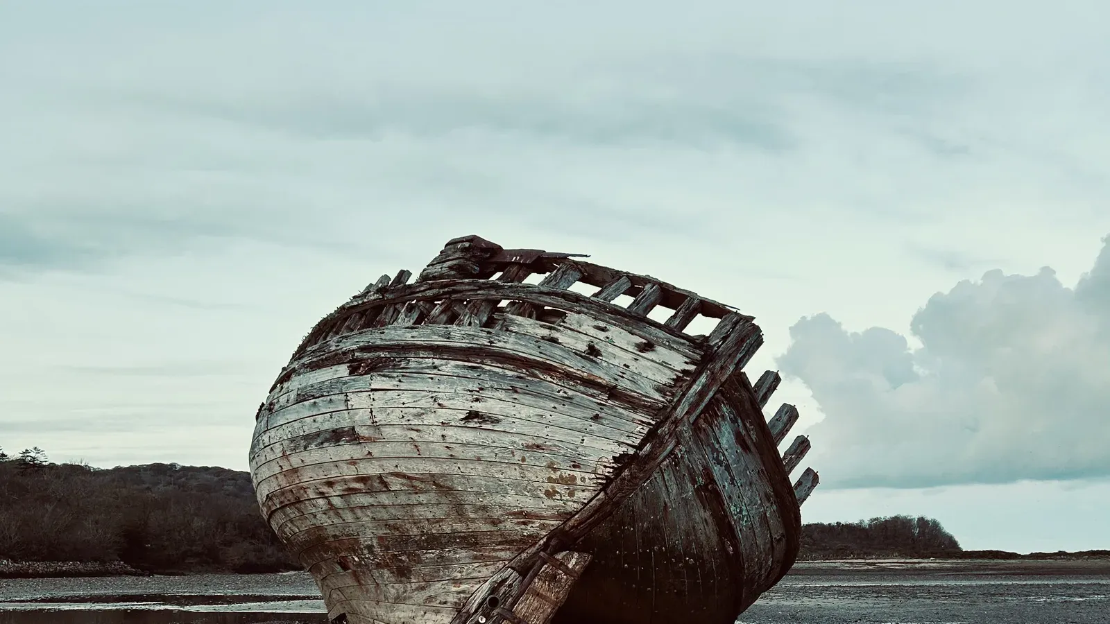 Weathered wooden shipwreck reflected in the wet sand at low tide on Traeth Dulas, Anglesey