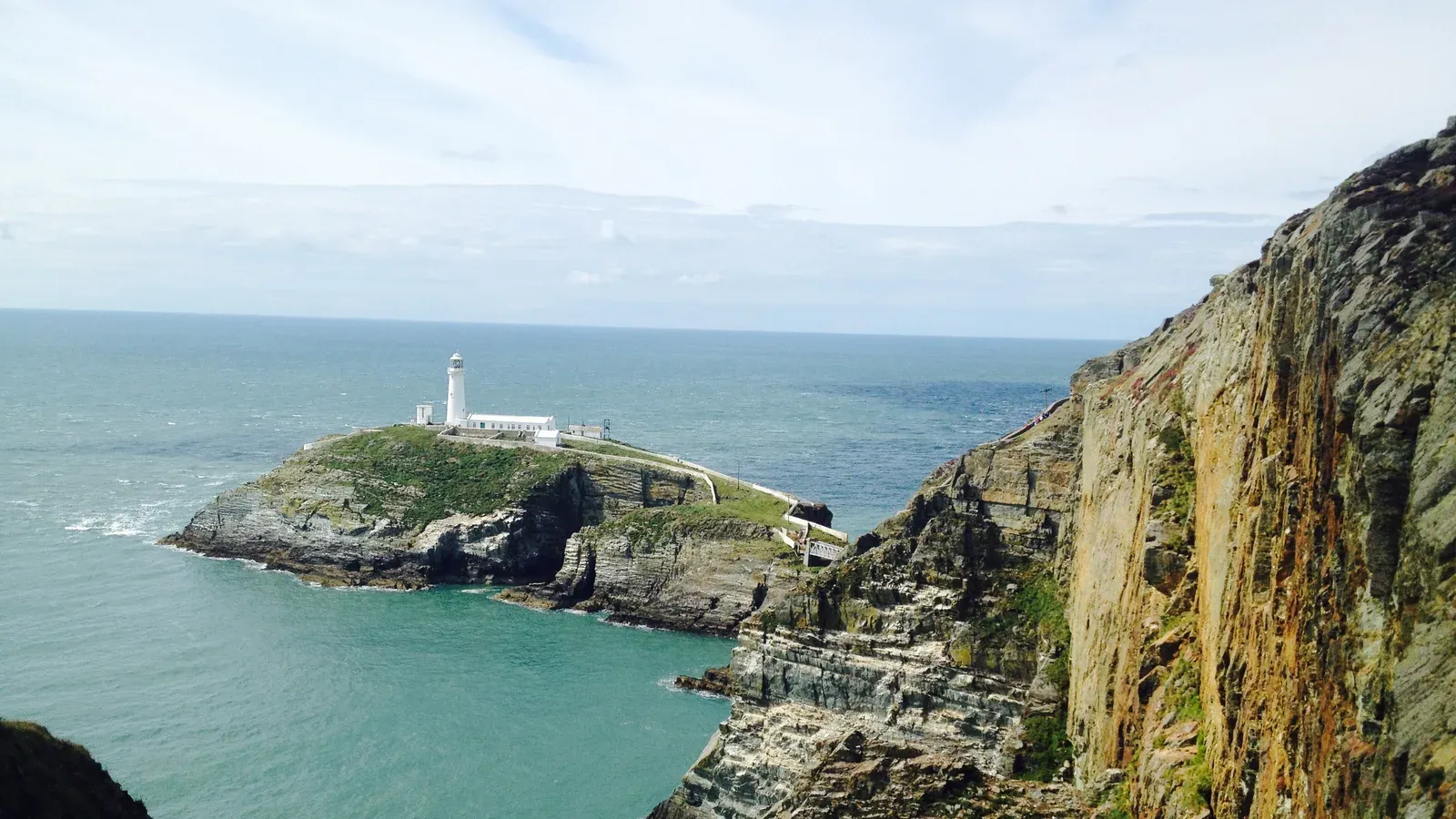 South Stack lighthouse on its islet off Holy Island, Anglesey, seen from the clifftop path above the layered sea cliffs