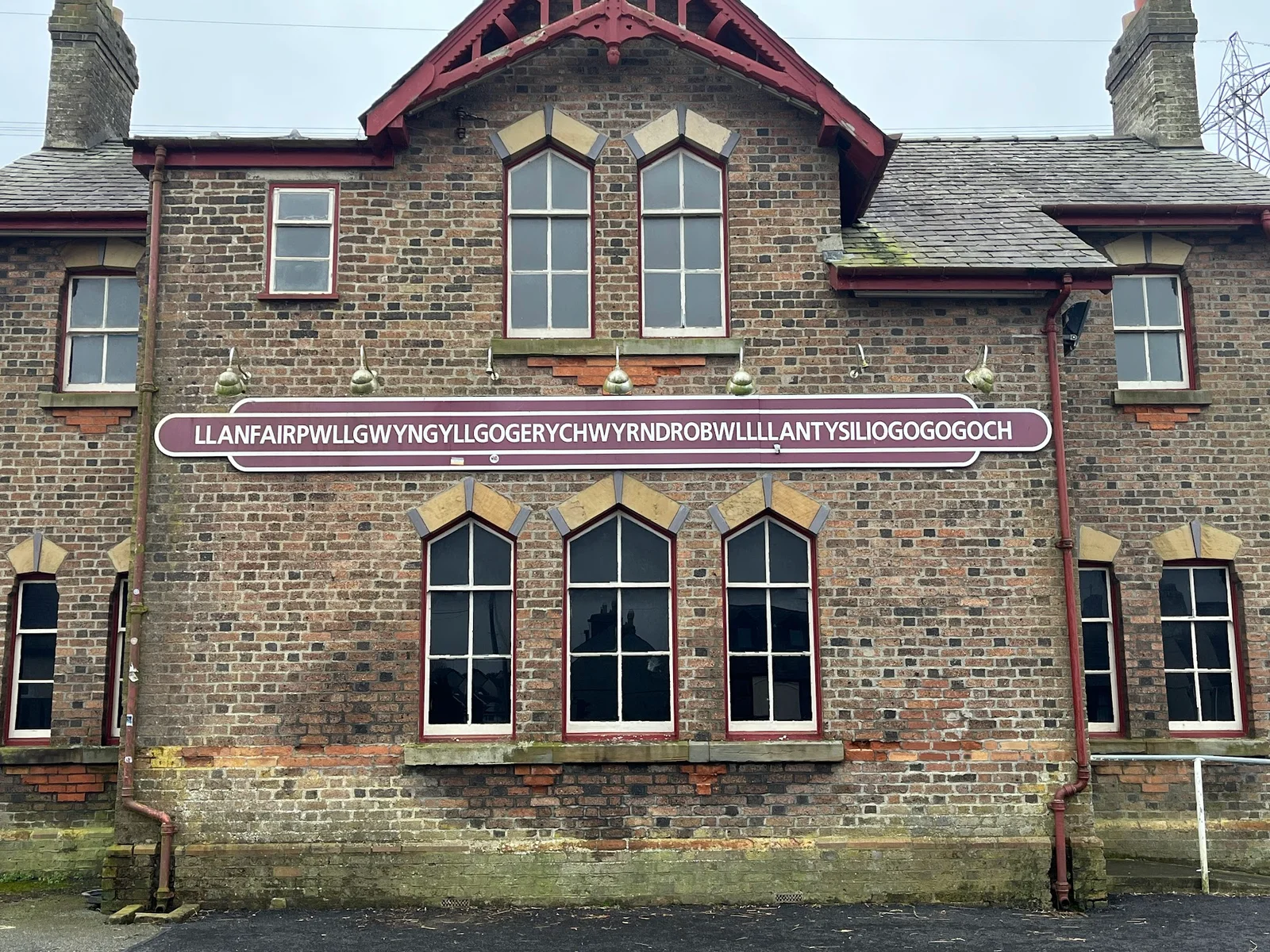 The famous long Llanfairpwll station name sign on the platform with visitors photographing it