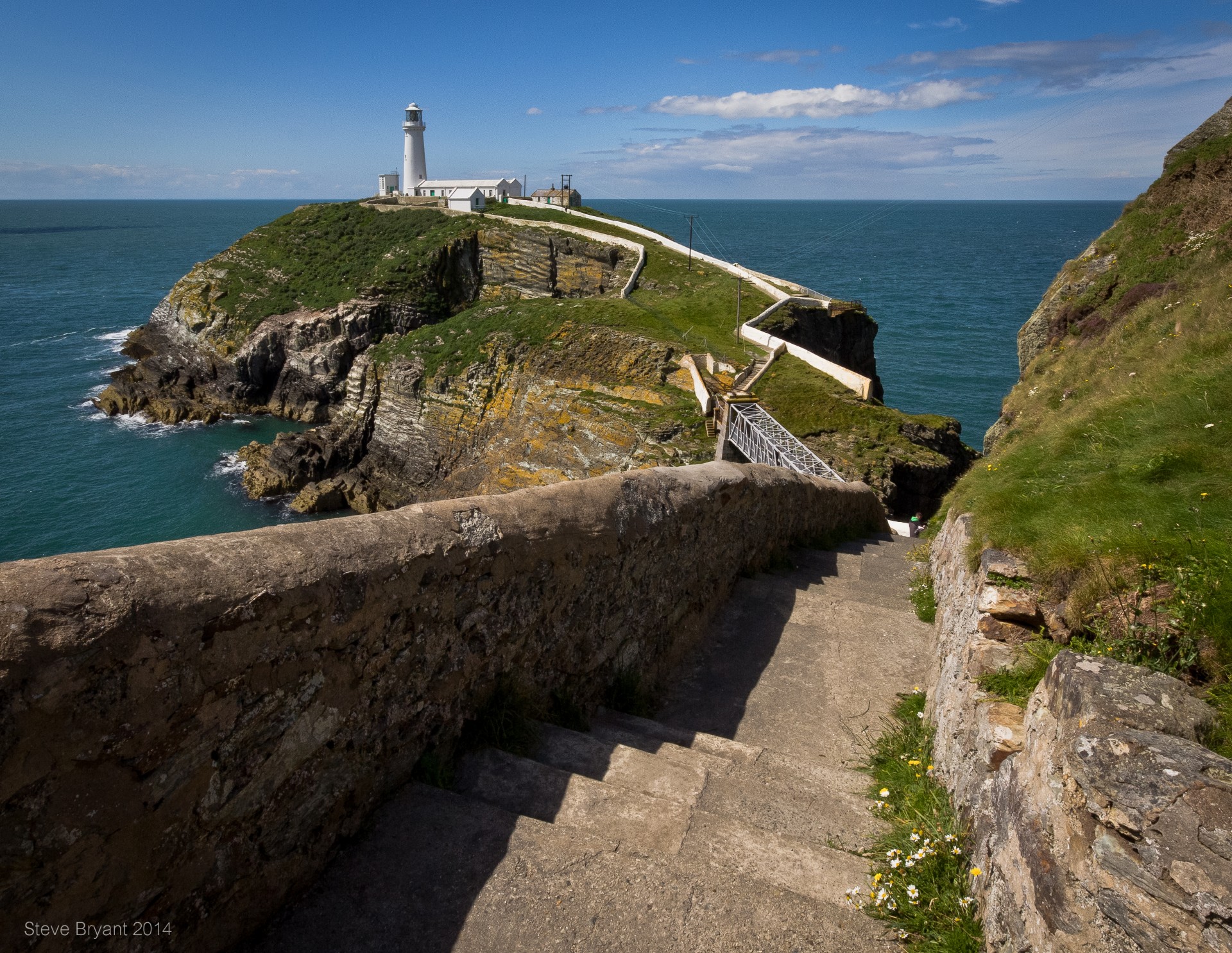 South Stack Lighthouse perched on its rocky islet off Holy Island cliffs, connected by a suspension bridge over churning seas